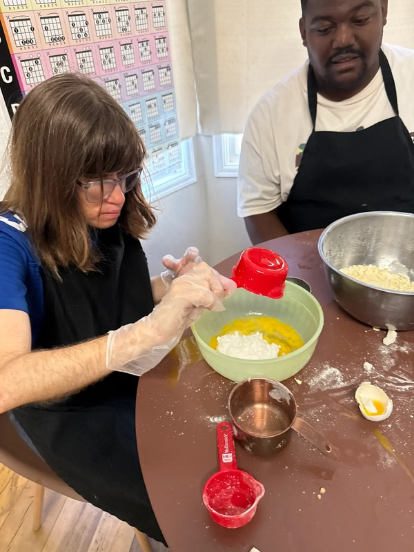 Adult with developmental disabilities measuring and mixing baking ingredients in green bowl during life skills cooking class at Ivey Ranch adult day program