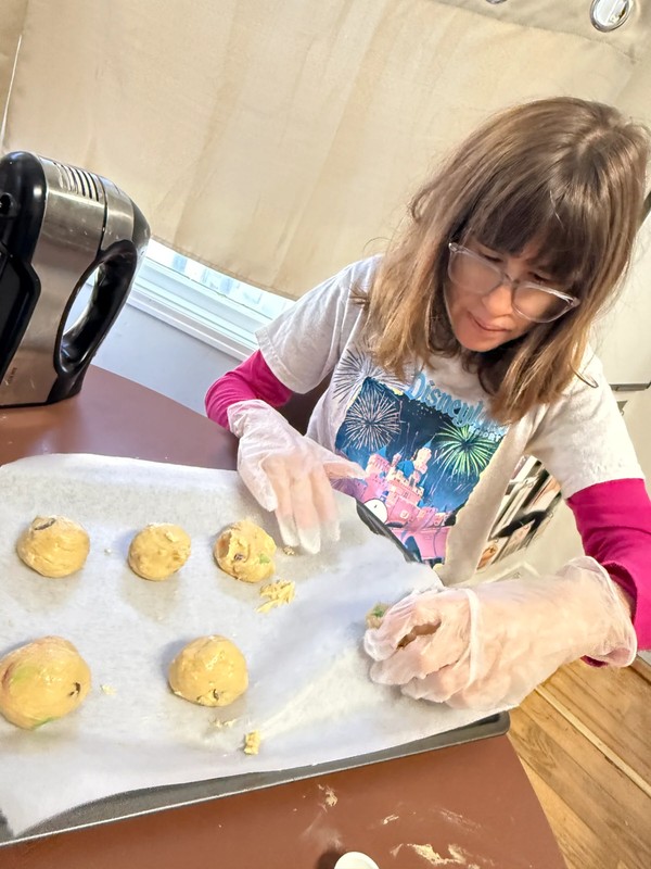 Young adult with special needs cracking eggs and preparing baking ingredients while wearing food safety gloves at day program kitchen table