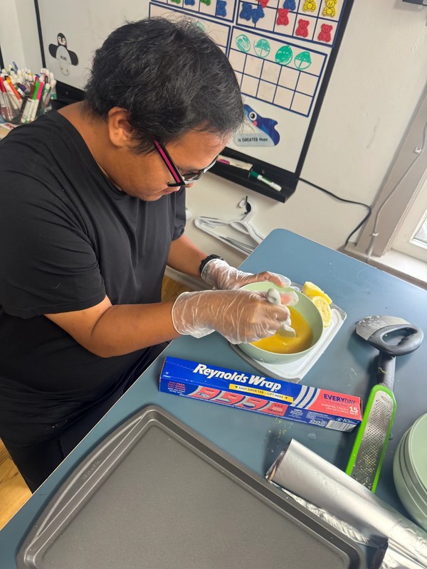 adult with special needs cracking eggs and preparing baking ingredients while wearing food safety gloves at day program kitchen table