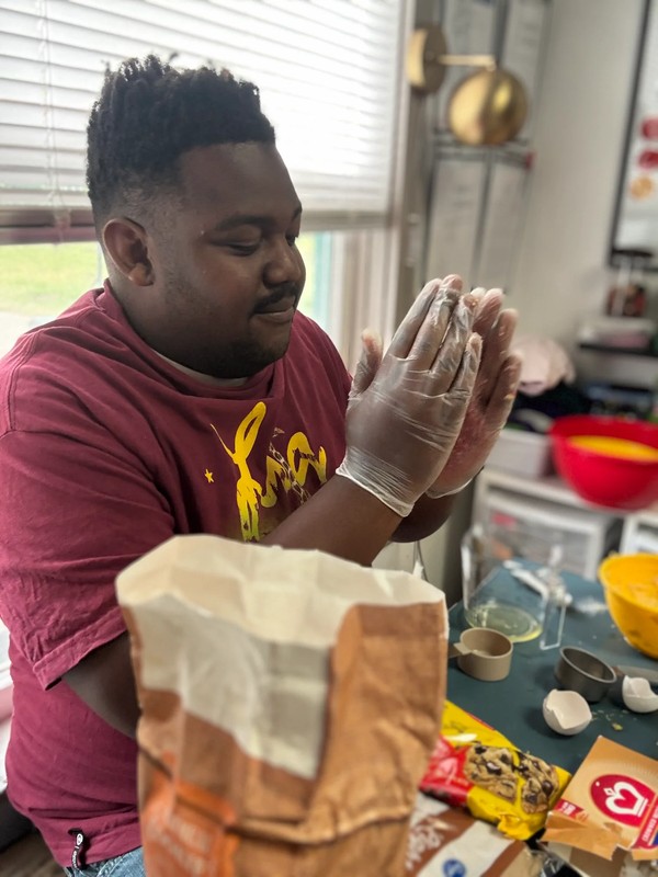 Group of adults with developmental disabilities working together around table forming and shaping cookie dough balls on baking sheet