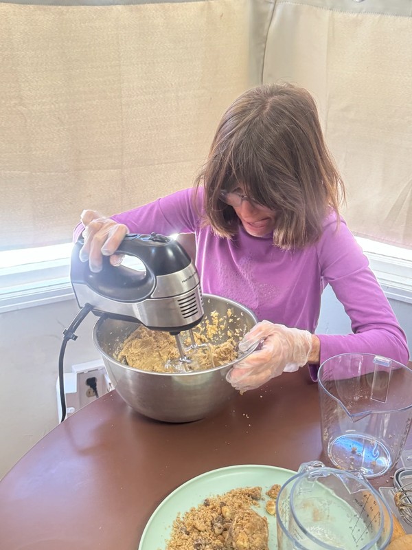 Woman with disabilities operating stand mixer with proper safety technique while mixing cookie dough in adult day program cooking class