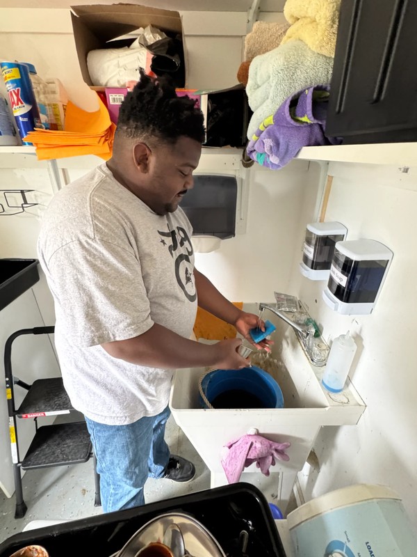Young adult with developmental disabilities washing dishes at sink and learning kitchen cleanup responsibilities at adult day program facility