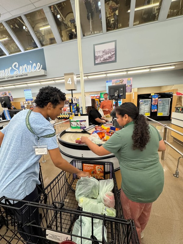 Two adult day program participants working together to place groceries on checkout counter, learning shopping skills and store etiquette at local supermarket with Ivey Ranch ADP