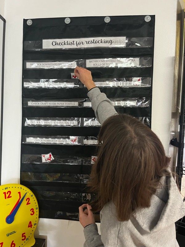 Adult day program participants using visual checklist to manage inventory and restock supplies, developing organizational and task management skills