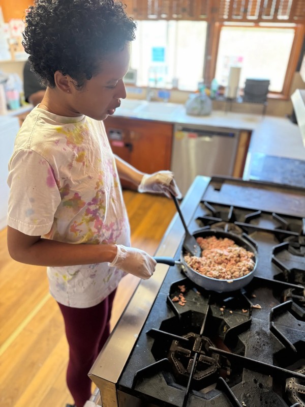 Adult with developmental disabilities learning to cook on a gas stovetop, practicing safe food preparation and independent meal-making skills
