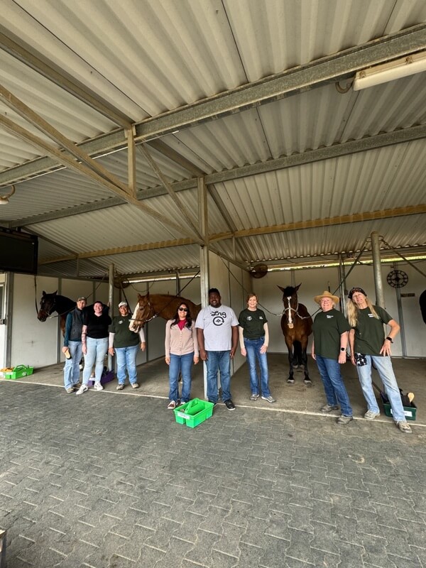 Group of adult day program participants and staff posing together with horses in stable