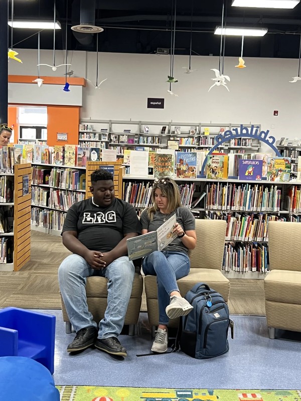 Adult day program participant with staff member reading together during library community outing