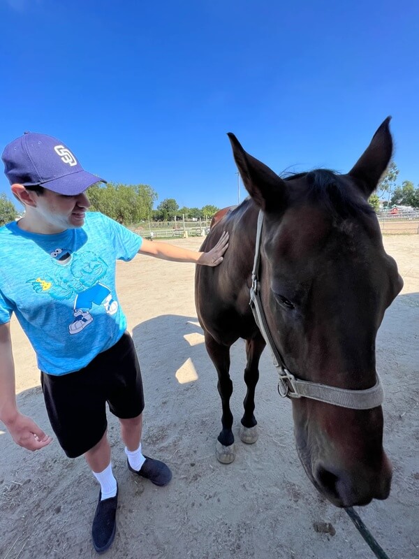 Participant wearing Padres cap petting brown horse outdoors at ranch on sunny day