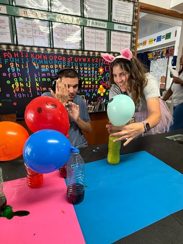 Two participants conducting balloon inflation science experiment with bottles and colored water