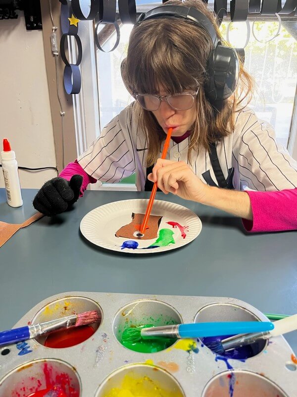 Participant wearing headphones using straw to blow paint in creative sensory art activity
