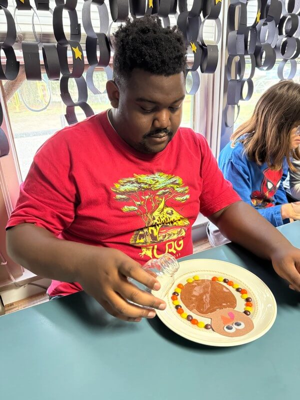 Adult creating colorful turkey craft on paper plate decorated with candy pieces