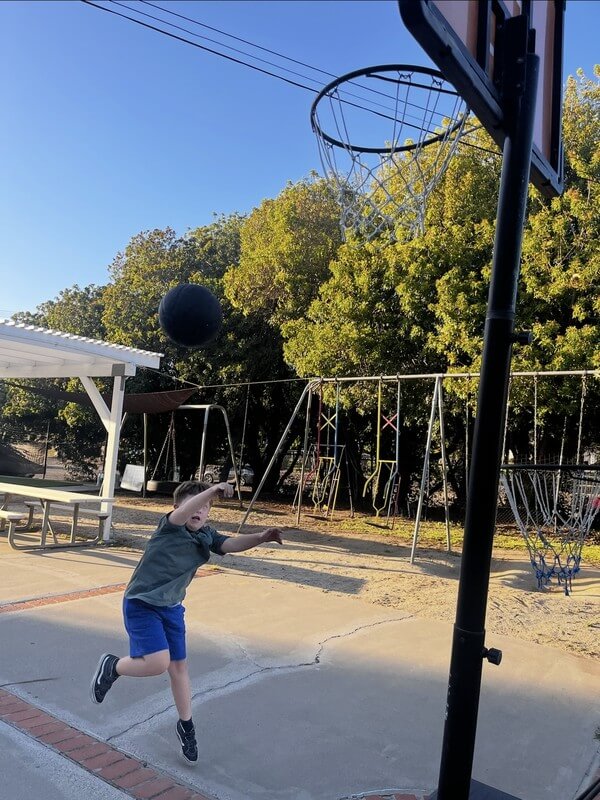 Child enjoying outdoor basketball activities at after-school care program, promoting physical activity and sports development in a safe playground environment.