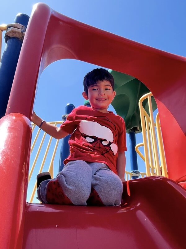Smiling boy enjoying outdoor play on colorful playground slide during school-age care, promoting active play and physical development.