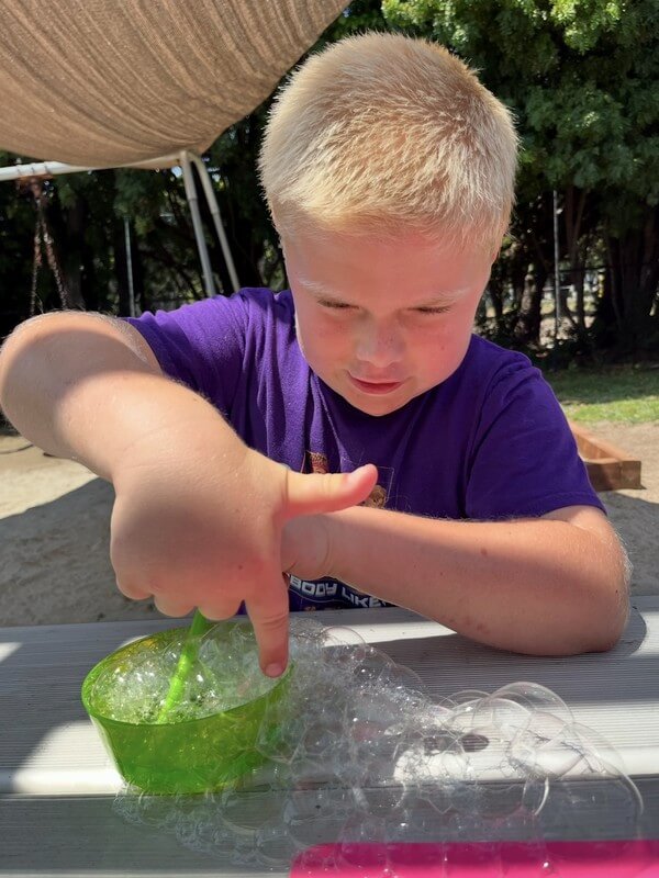 Boy engaged in hands-on sensory play with green slime experiment at after-school care, promoting tactile learning and scientific exploration.