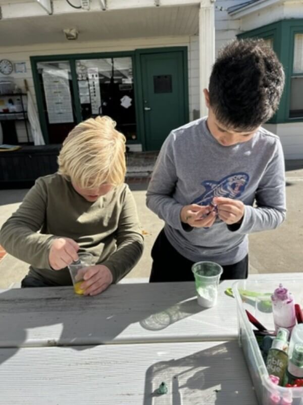 Children collaborating on science experiment making colorful slime at school-age program, fostering teamwork and STEM learning through hands-on activities.