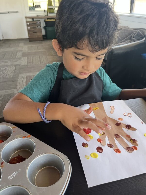 Young child making handprint art with autumn colors during creative activity at daycare, developing artistic skills and self-expression through painting.