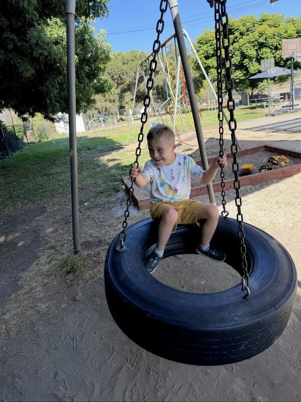 Smiling child playing on tire swing during outdoor recreation time at school-age program, promoting balance, coordination, and active play.