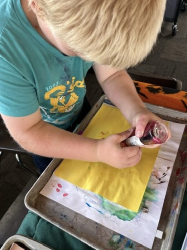 Young child doing stamping art project on yellow paper at after-school program, exploring creativity and color mixing through hands-on activities.