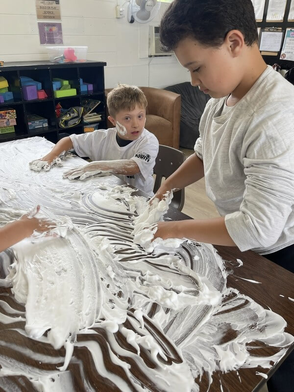 Two children engaged in messy sensory play with cream during art time at school-age care, promoting tactile exploration and creative expression.