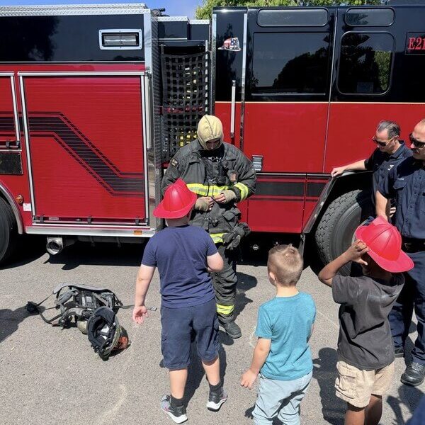 Kids participating in fire safety education with local firefighters at after-school program, learning about community helpers and safety awareness.