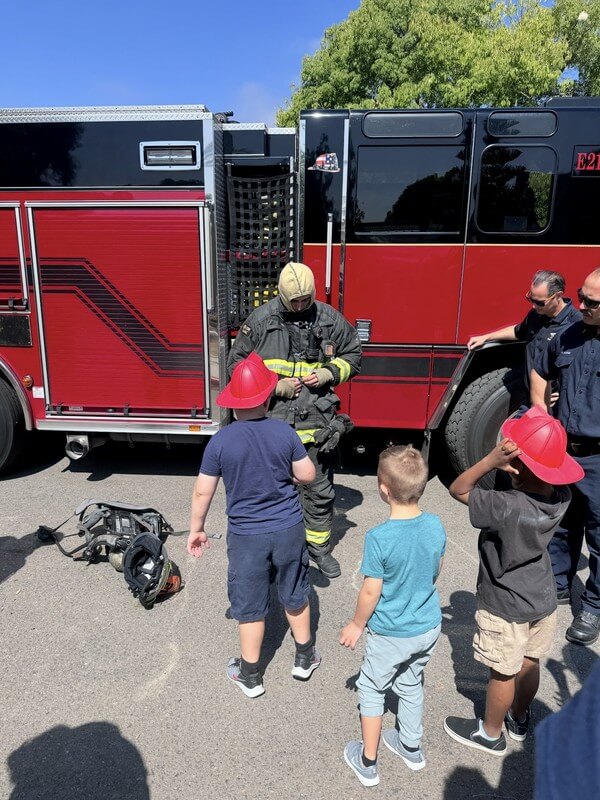 Kids participating in fire safety education with local firefighters at after-school program, learning about community helpers and safety awareness.