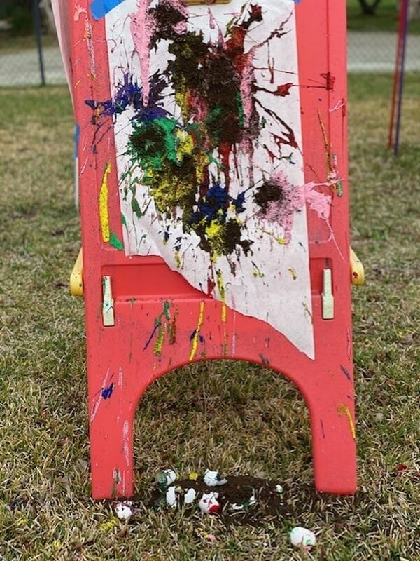 Colorful abstract splatter paint artwork displayed on red easel outdoors at Ivey Ranch after-school program
