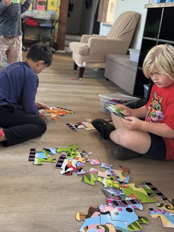 Two boys sitting on floor working together to complete bright colorful floor puzzle with various shaped pieces