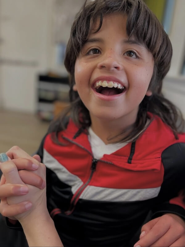 Close up of happy child in red and black striped shirt with big smile during school age program indoor playtime
