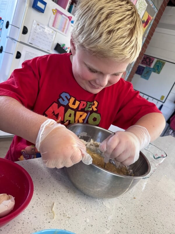 Boy wearing food safe gloves mixing cookie dough by hand in metal bowl during baking activity