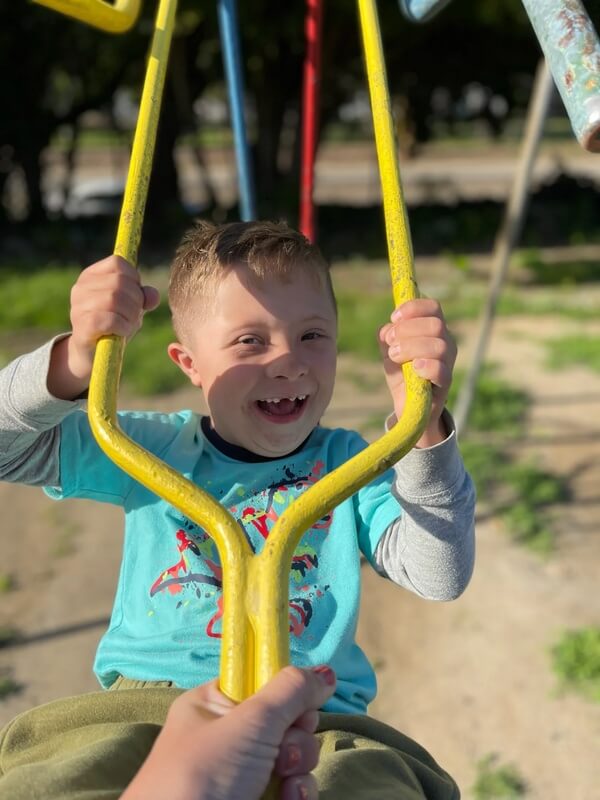 Excited young child in turquoise shirt holding yellow swing chains and laughing on playground equipment