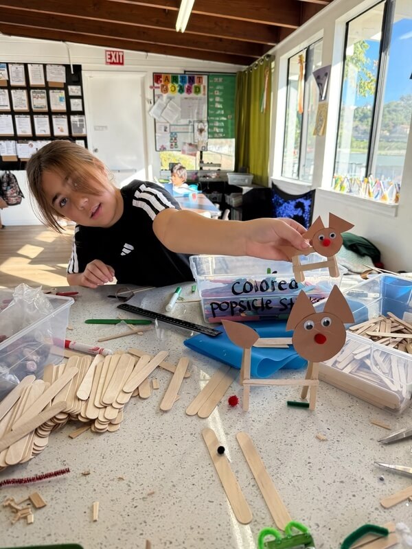 Young student proudly displaying handmade animal craft made from popsicle sticks and construction paper