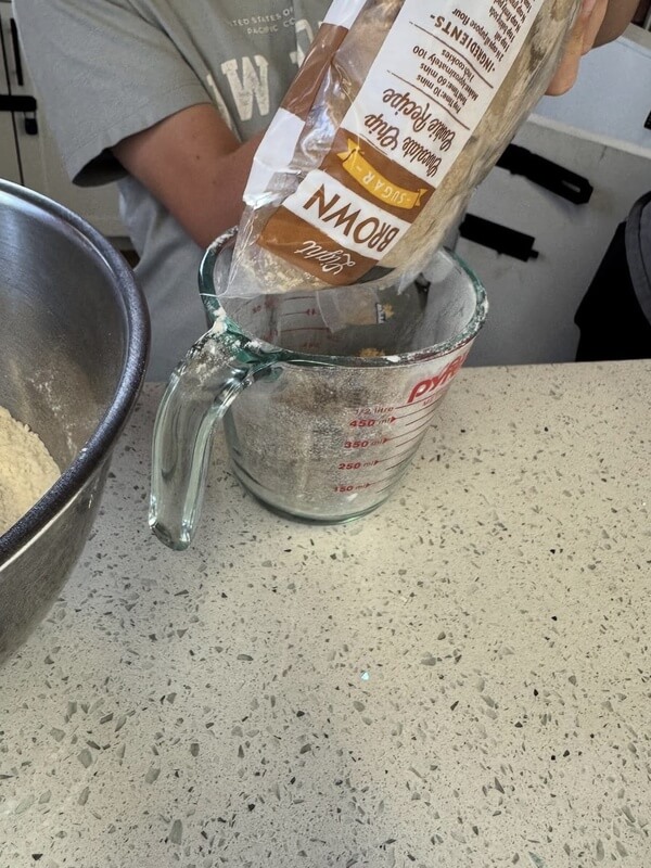 Close up of hands pouring brown sugar from bag into glass measuring cup during precise baking measurement activity