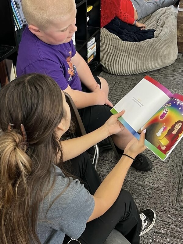 Program staff reading colorful storybook with boy in purple shirt during one on one reading time in cozy corner area