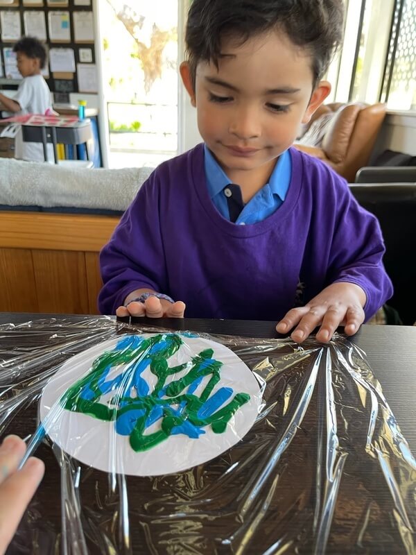 Child engaging in sensory art experience painting on paper plate covered with plastic wrap