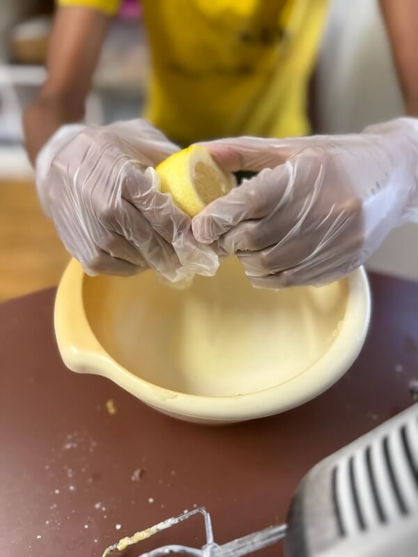 Hands wearing food safe gloves squeezing fresh lemon half over yellow bowl during cooking and food prep lesson
