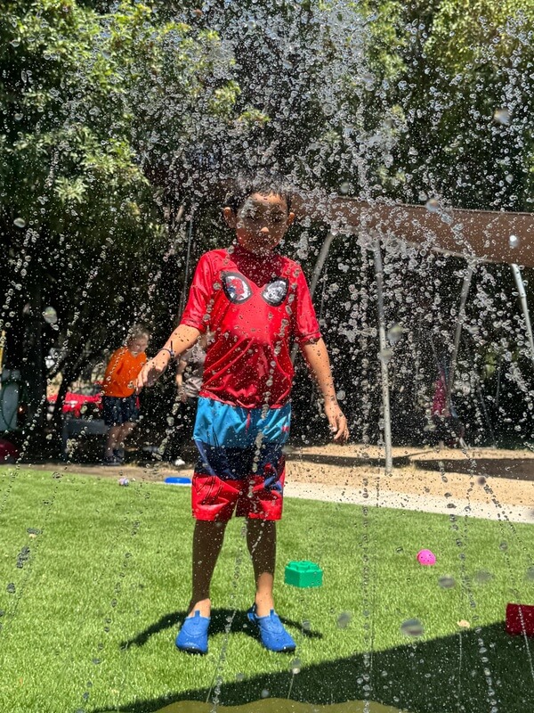 Child standing in sprinkler spray getting soaked during outdoor water play time