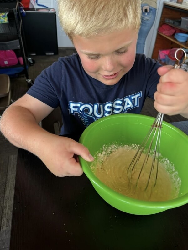 Boy concentrating while whisking baking ingredients in bright green bowl learning mixing techniques during after school cooking class