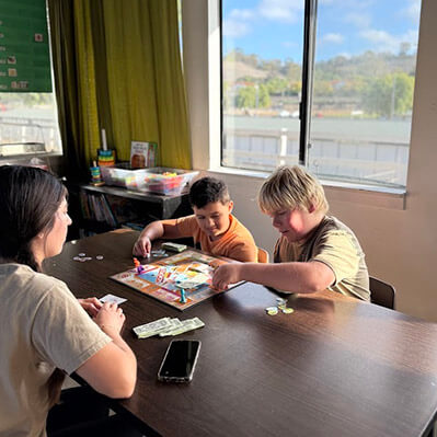 A childcare intern playing a board game with two children at Ivey Ranch Park Association's inclusive childcare program in Oceanside, California