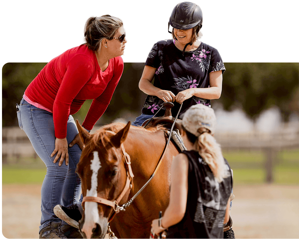 An Ivey Ranch riding instructor guides a therapeutic riding participant on horseback while a sidewalker provides support at Ivey Ranch Park Association in Oceanside, CA