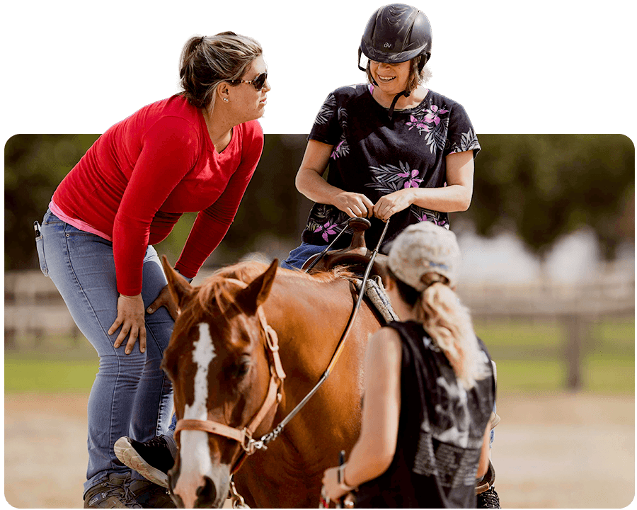 An Ivey Ranch riding instructor guides a therapeutic riding participant on horseback while a sidewalker provides support at Ivey Ranch Park Association in Oceanside, CA