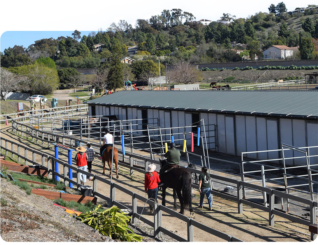 Volunteers and instructors leading riders on horseback through the therapeutic riding arena at Ivey Ranch Park Association in Oceanside, California