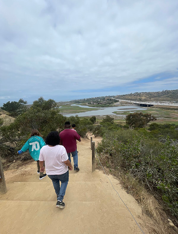 Ivey Ranch Adult Day Program participants climbing stairs on a coastal trail overlooking a lagoon and the Pacific Ocean