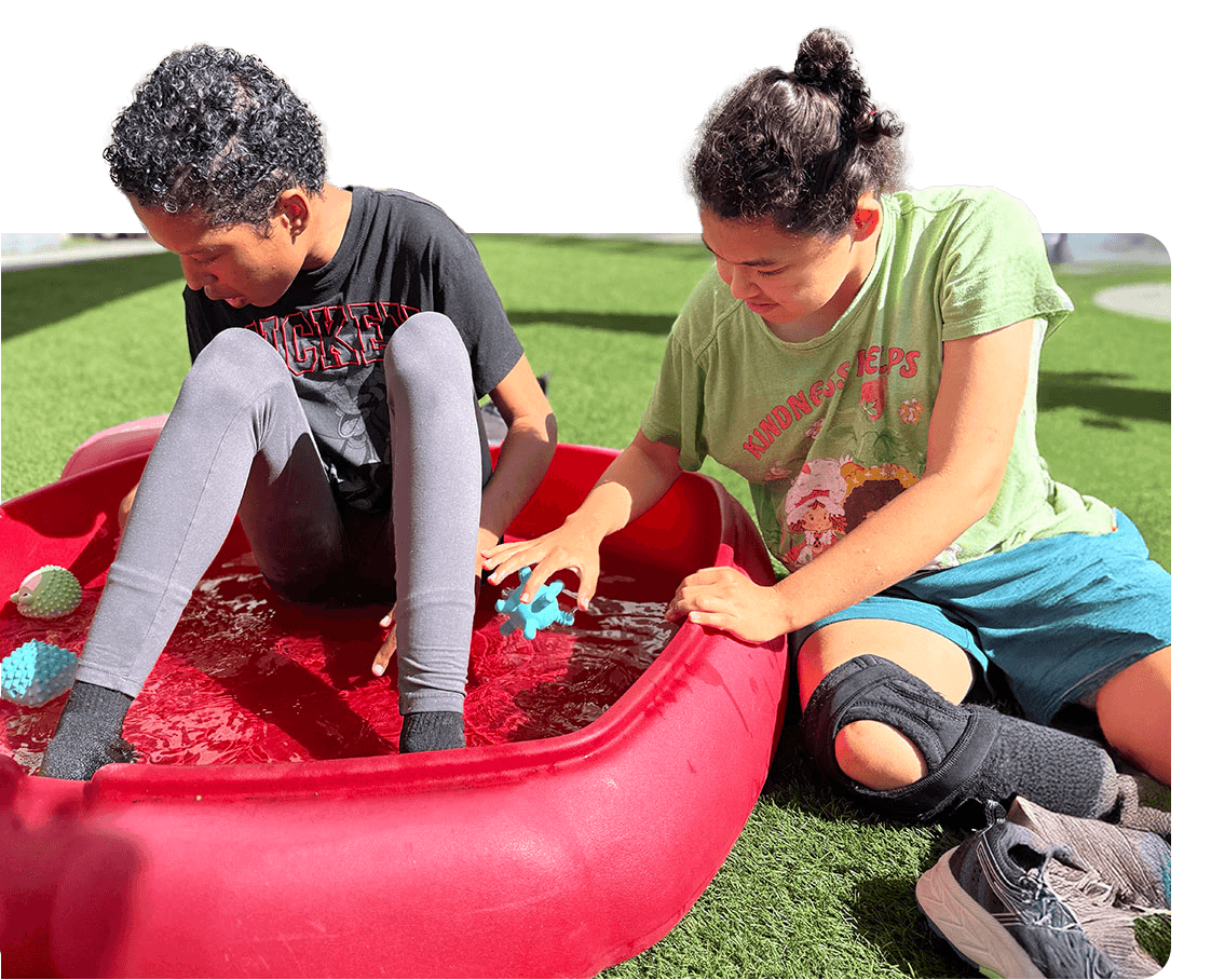 Two girls in the Ivey Ranch care program playing in a sensory pool during a childcare session