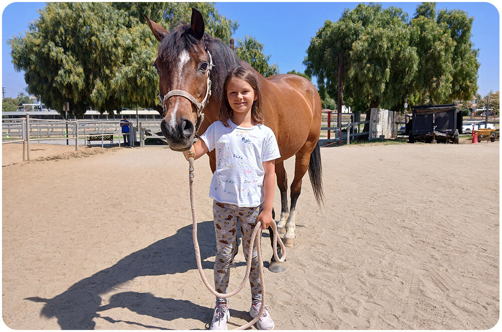 A young girl holds the horse by the rope in the Ivey Ranch arena during a birthday party horse experience in Oceanside, CA.