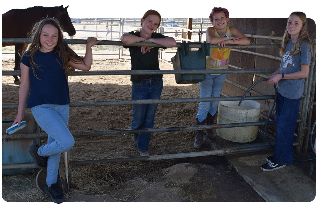 Four girls smile and pose along a barn fence at Ivey Ranch during a Scout Program session in Oceanside, CA.