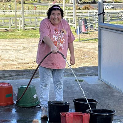 Tailored Day Service participant filling water buckets during barn chores at Ivey Ranch in Oceanside, CA