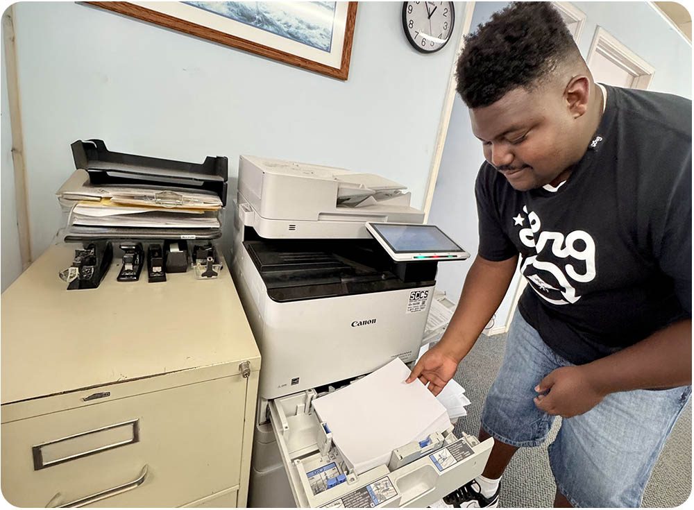 Tailored Day Service participant loading paper into a copy machine during office skills training at Ivey Ranch in Oceanside, CA