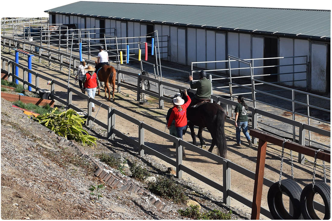 Riders and volunteers leading horses through the riding arena at Ivey Ranch in Oceanside, CA