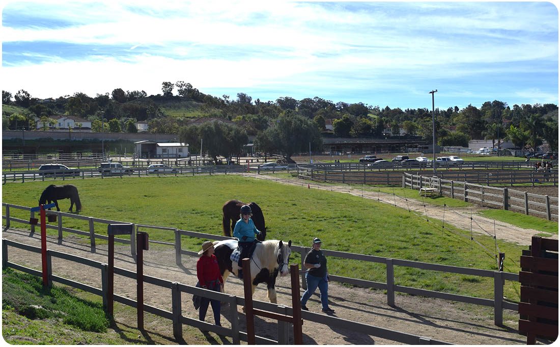 Volunteers leading a horse and rider through the pasture at Ivey Ranch in Oceanside, CA